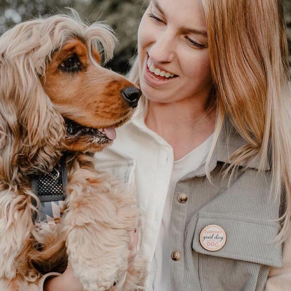 A woman wearing a wooden dog pin holding her sable Cocker Spaniel and smiling
